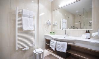 A modern bathroom with a large mirror and an elegant bathtub. Towels are neatly hung, and there is a small shelf with toiletries.