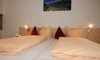 A cozy bedroom with two beds and red cushions. A picture of a mountain landscape hangs on the wall.