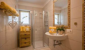 A modern bathroom with a shower and bright tile design. Yellow towels are placed on the sink, and a small plant creates a pleasant atmosphere.