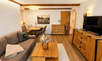 A modern living room with wooden furniture and a cozy sofa. An artwork depicting a mountain landscape hangs on the wall.