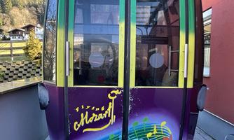 A colorful gondola with a music concept named "Mozart". It stands on a paved floor and is surrounded by a modern building.