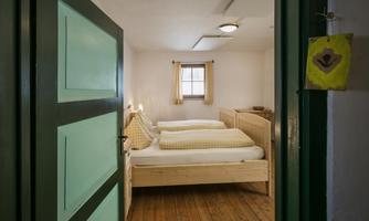 A cozy bedroom with two beds and hardwood floors. Soft lighting conditions through a window and subtle decoration.