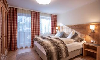 A cozy bedroom with a large bed and decorative pillows. Bright curtains and wooden details create a warm atmosphere.