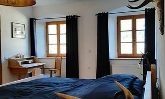 A cozy bedroom with a large bed and a wooden frame. The windows offer a view of nature, and the room is decorated with an elegant lamp and deer antlers.