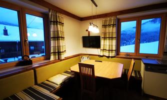 A cozy kitchen with a wooden farmhouse table and a large window. Outside, snow can be seen and the atmosphere is warm and inviting.
