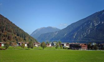 A picturesque landscape with green meadows and mountains in the background. Small houses adorn the valley under a clear blue sky.