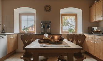 A cozy kitchen with wooden furniture and large windows. A table with fruit and candles creates an inviting atmosphere.