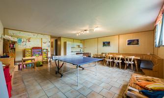 A spacious room with a table tennis table and a seating area. Pictures hang on the walls, and there are toys and furniture for children.