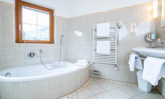 A modern bathroom with a bathtub and a large window. Towels hang on a radiator and the decor is bright and friendly.