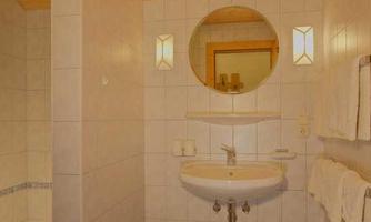 A modern bathroom with white tiles and a round mirror. The sink area is brightly lit and well-organized.