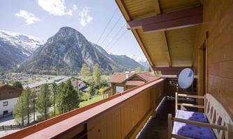 A balcony with a view of an impressive mountain landscape. The sun is shining, and the surroundings are calm and idyllic.