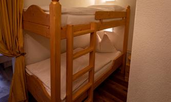 A wooden bunk bed stands in a cozy room. The walls are bright and a curtain made of yellow fabric hangs at the window.