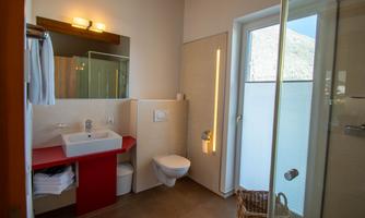 A modern bathroom featuring a shower and a sink on a red vanity. Large windows let in plenty of light and offer a view outside.