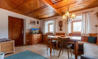 A cozy living room with wooden paneling and a large table. There is a sofa, a TV corner, and a warm atmosphere.