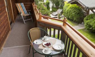 A cozy balcony with a small table and two coffee cups. In the background, a beautiful garden can be seen.