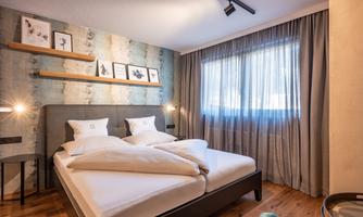A modern bedroom with a double bed and bright curtains. Decorative pictures hang on the wall, and the room has a warm wooden floor.