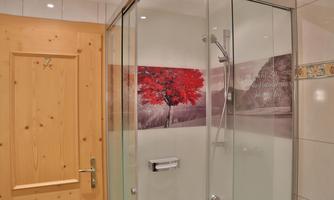 A modern bathroom with a glass shower. On the wall is a large picture of a red tree against a scenic backdrop.