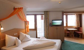 A cozy hotel room with a large bed and white pillows. There is a television and a dining area with a table.