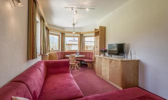 A cozy living room with red sofas and a large window. A table with chairs and a television complete the furnishings.