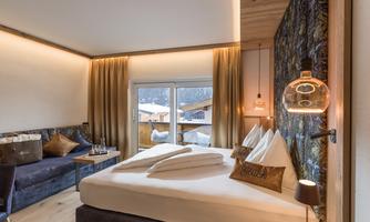 A modern hotel room with a cozy double bed and an attractive seating area. Large windows offer a view of the snowy landscape.