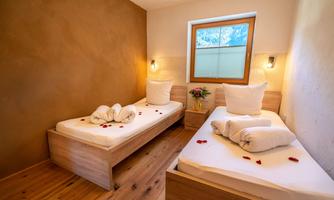 A cozy room with two single beds and wooden details. Rose petals and a flower vase create a romantic atmosphere.