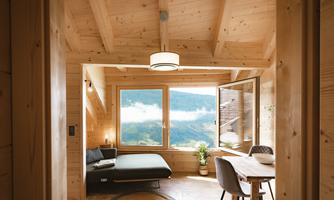 A modern wooden room with large windows and a view of the mountains. There is a cozy seating area and a small table.