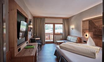 A modern hotel room with wooden paneling and a large window. It offers a view of the surroundings and is cozily furnished.