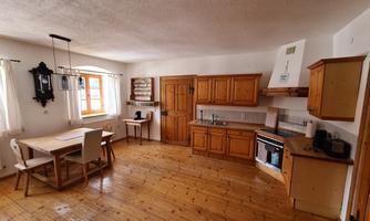 A cozy kitchen with wooden cabinets and a dining table. The room has large windows that let in plenty of light.