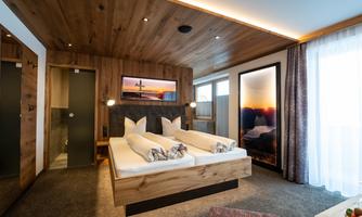 A modern hotel room with wooden details and two beds. Large windows provide a bright space with a cozy atmosphere.