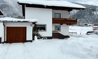 A beautiful house in the snow with a garage door. The surroundings are wintry and surrounded by mountains.