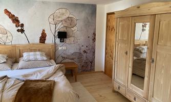 A cozy bedroom with a large bed and wooden furniture. The wall is decorated with a floral-inspired wallpaper.