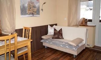A cozy living room with a white sofa and decorative cushions. A dining area with wooden chairs and a table is also available.