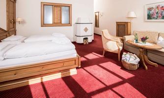 A cozy hotel room with a double bed and a comfortable armchair. The room is brightly lit and features a warm, inviting carpet.