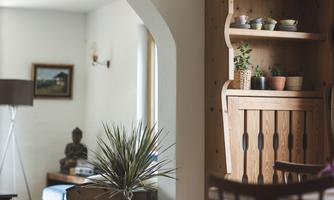 A cozy room with a wooden box, plants, and a Buddha statue. The walls are light and the light streams through the window.