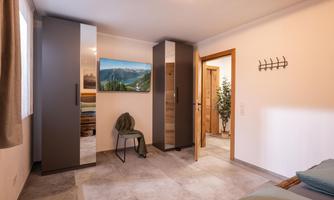 A modern bedroom with a wardrobe and a chair. A picture of a mountain landscape is hanging on the wall.