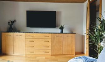 A modern living room with a wooden cabinet, a television on the wall, and a plant on the table. The atmosphere feels bright and inviting.