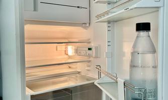 An empty refrigerator with a clear bottle and few shelves. The interior light is on and the refrigerator is tidy.