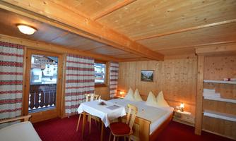 A cozy room with wooden paneling and a large window. Two beds and a table with chairs invite you to relax.