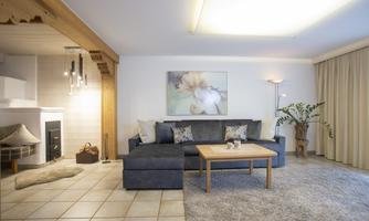 A modern living room with a cozy couch and a wooden table. The room is brightly lit and has a friendly, welcoming atmosphere.
