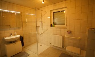 A modern bathroom with a glass shower and bright tiles. There is a sink, a toilet, and a window for daylight.