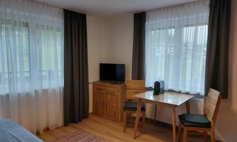 A bright room with large windows and curtains.  
In the room are a table with chairs, a television, and a wooden cabinet.