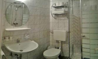 A small bathroom with a shower cabin, a sink, and a toilet. The walls are tiled with light tiles.