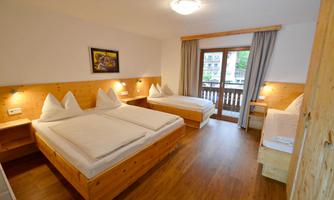 A cozy room with two beds and a window to the balcony door. The wooden decorations and pleasant light create an inviting atmosphere.