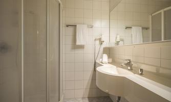 A modern bathroom with a shower cabin and a round sink. The walls are tiled and there are fresh towels.