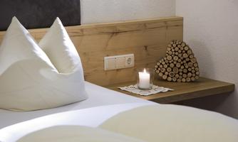 A cozy bedroom with a wooden board and a burning candle. The pillows are arranged in an appealing shape and a wooden sculpture stands on the table.