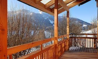 A cozy wooden terrace with a view of snow-covered mountains. The sun is shining and the sky is clear.