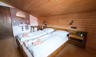 A cozy bedroom with two single beds and wooden paneling. The room is bright and modernly designed, featuring a small sink and a plant on the nightstand.