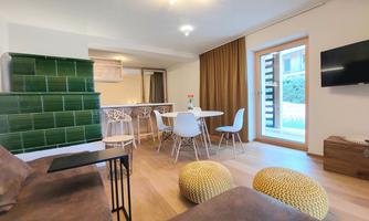 A cozy interior view with a modern dining area and a small kitchen. The room is bright and friendly, with a view of a garden through the windows.