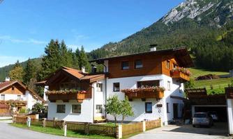 A charming house in alpine style with balconies and flowers. In the background, green mountains and a clear sky can be seen.