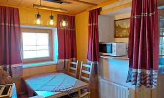 A cozy kitchen with a wooden table and chairs. Red curtains and a microwave complete the space.